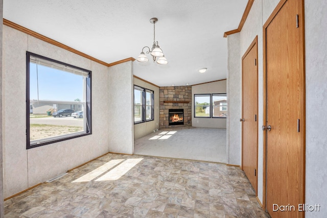 unfurnished living room featuring crown molding, a stone fireplace, and a chandelier