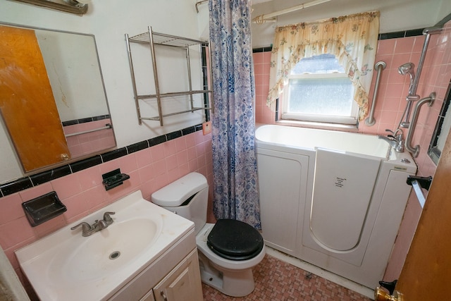 bathroom featuring toilet, vanity, tile walls, and independent washer and dryer