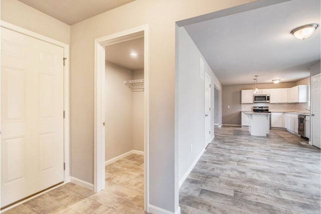 kitchen with appliances with stainless steel finishes, pendant lighting, a center island, light hardwood / wood-style floors, and white cabinetry