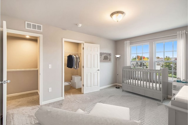 bedroom with ensuite bath, a spacious closet, light carpet, a closet, and a crib