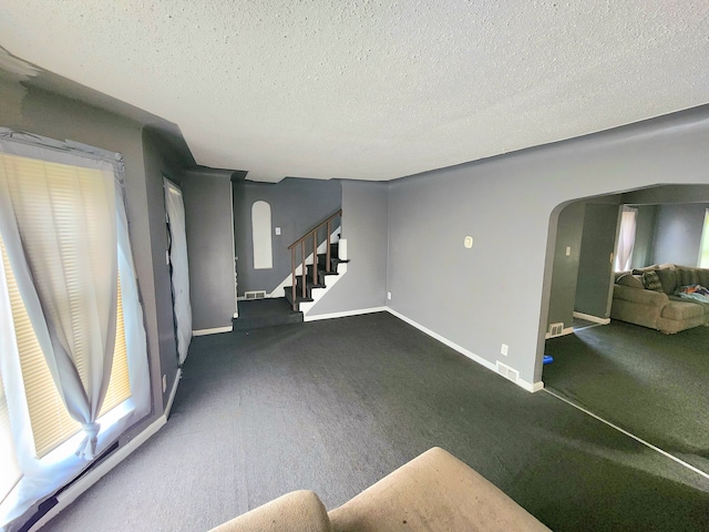 unfurnished living room featuring dark colored carpet and a textured ceiling