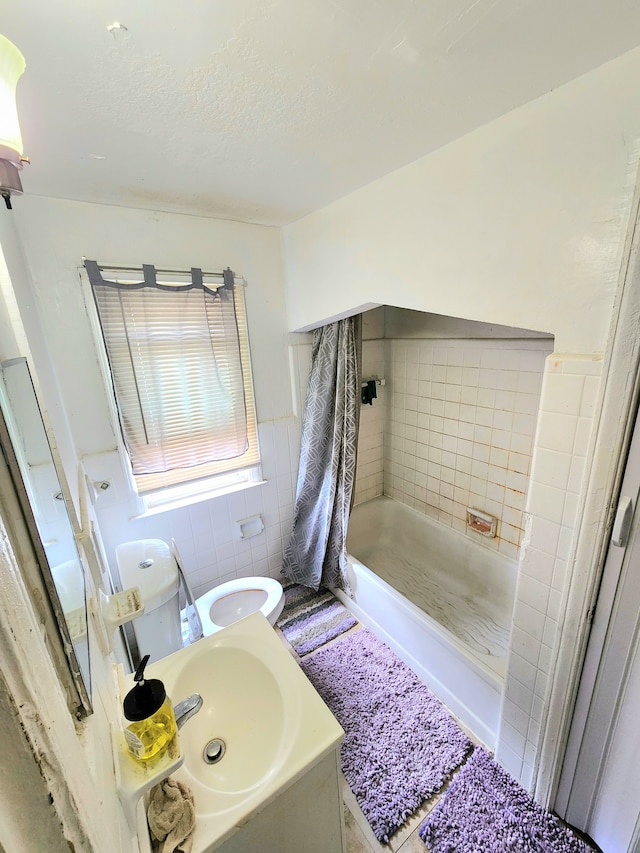 bathroom featuring tiled shower, vanity, toilet, and tile walls