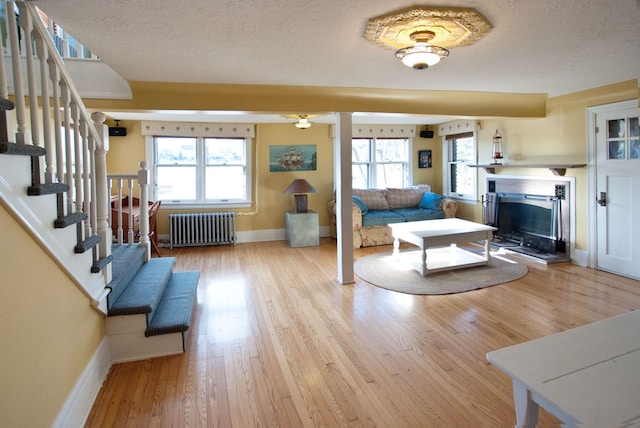 living room featuring radiator, light hardwood / wood-style flooring, a healthy amount of sunlight, and a textured ceiling