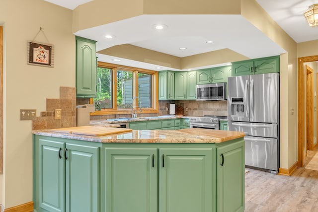 kitchen with green cabinets, kitchen peninsula, light hardwood / wood-style floors, decorative backsplash, and appliances with stainless steel finishes