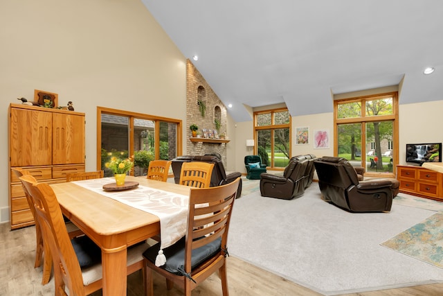 dining space featuring a fireplace, plenty of natural light, high vaulted ceiling, and light wood-type flooring