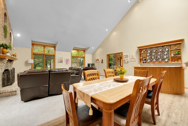 dining area featuring a fireplace, high vaulted ceiling, and light wood-type flooring