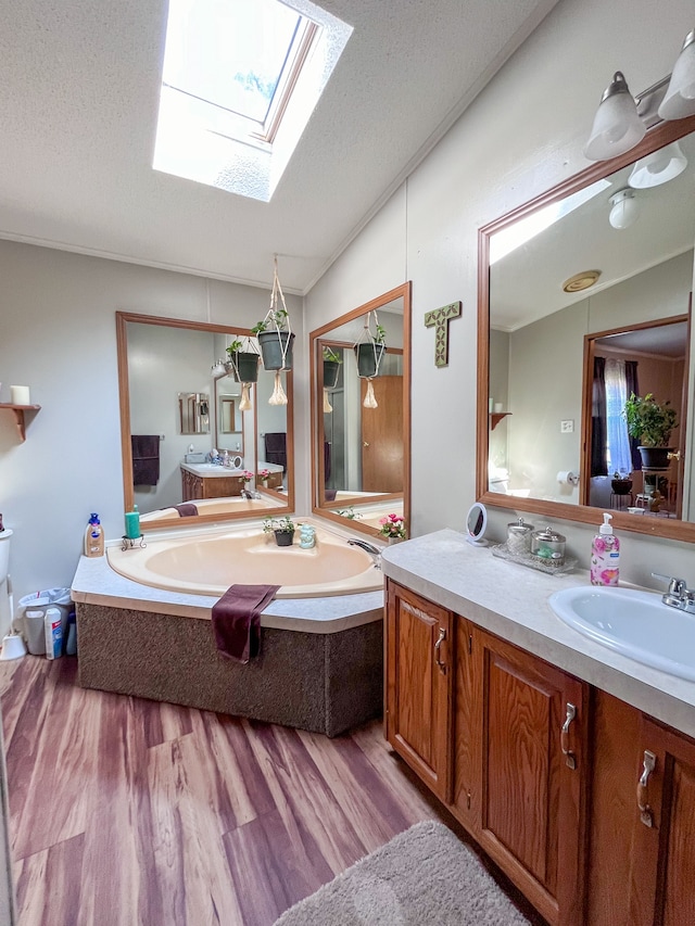 bathroom featuring hardwood / wood-style floors, vanity, vaulted ceiling with skylight, and a textured ceiling