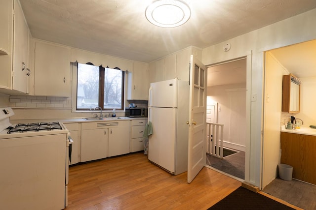 kitchen featuring decorative backsplash, white appliances, light wood-style floors, and a sink