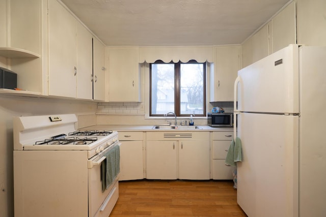 kitchen with white appliances, a sink, light countertops, light wood-type flooring, and backsplash