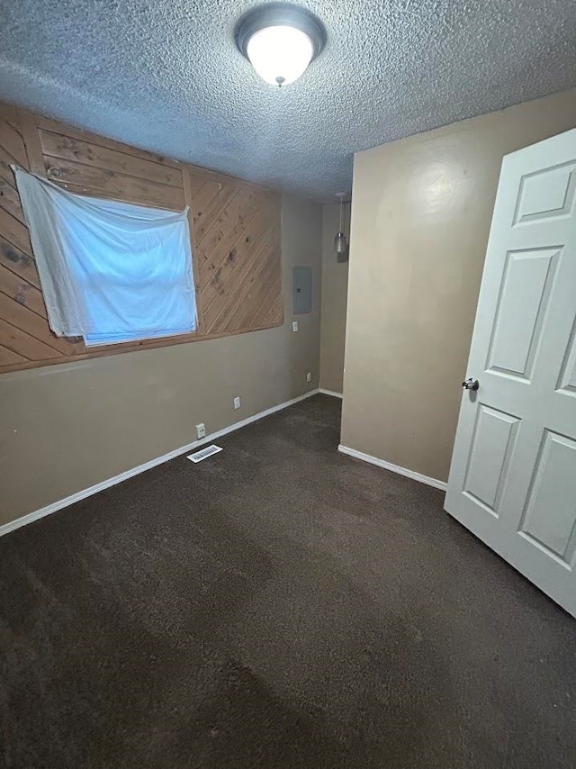 carpeted spare room featuring electric panel, wooden walls, and a textured ceiling