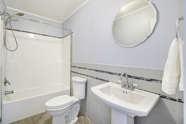 full bathroom with sink, a textured ceiling, toilet, shower / bathing tub combination, and tile walls