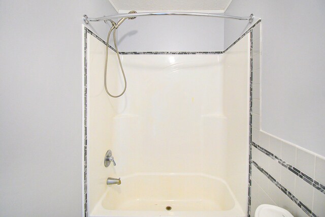 bathroom featuring washtub / shower combination and tile walls