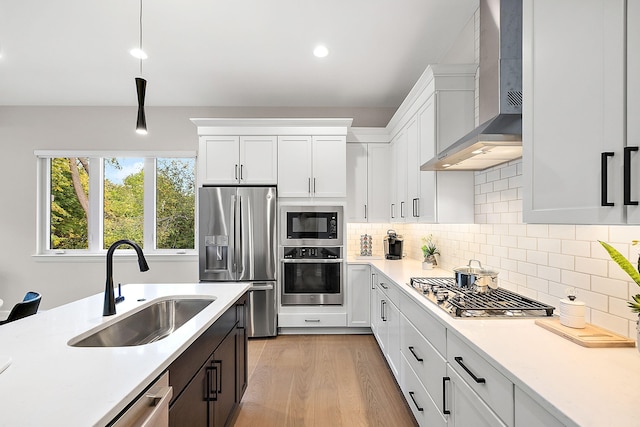 kitchen featuring wall chimney exhaust hood, stainless steel appliances, sink, decorative light fixtures, and white cabinetry