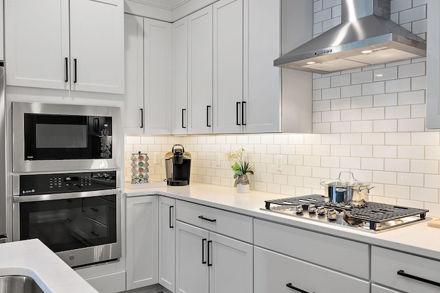 kitchen with white cabinets, backsplash, wall chimney range hood, and stainless steel appliances