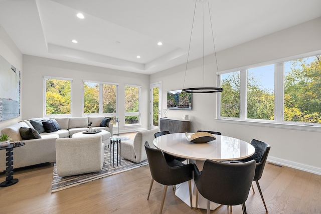 dining area featuring light wood-type flooring and a raised ceiling