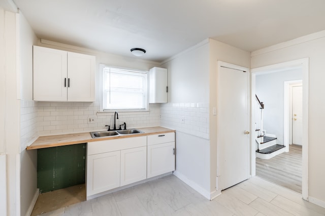 kitchen featuring crown molding, sink, light hardwood / wood-style flooring, white cabinetry, and butcher block counters