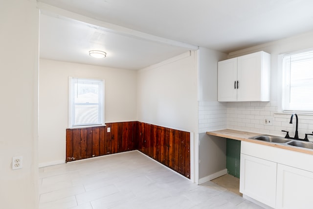 kitchen with wood walls, backsplash, white cabinets, sink, and butcher block counters