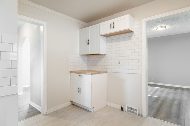 kitchen featuring white cabinets, light hardwood / wood-style floors, backsplash, and wooden counters