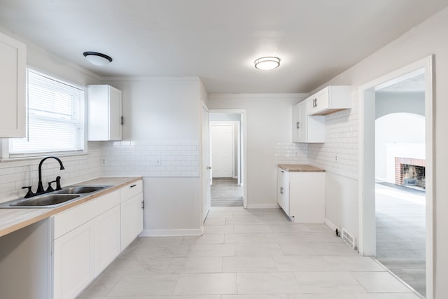 kitchen with white cabinets, decorative backsplash, butcher block counters, and sink