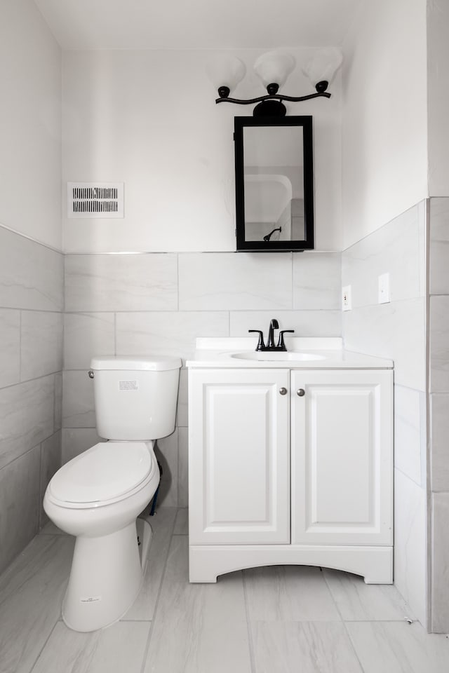 bathroom featuring vanity, toilet, and tile walls