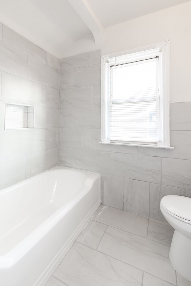 bathroom with a bath, toilet, and tile walls