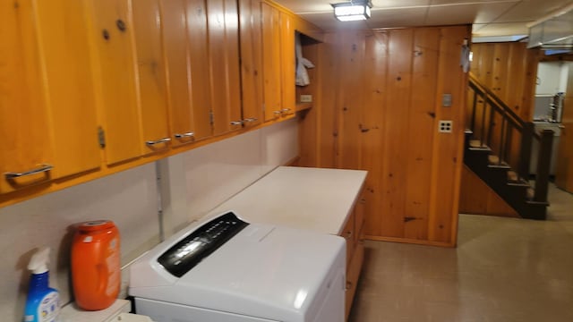 clothes washing area featuring cabinets, wood walls, and washing machine and dryer