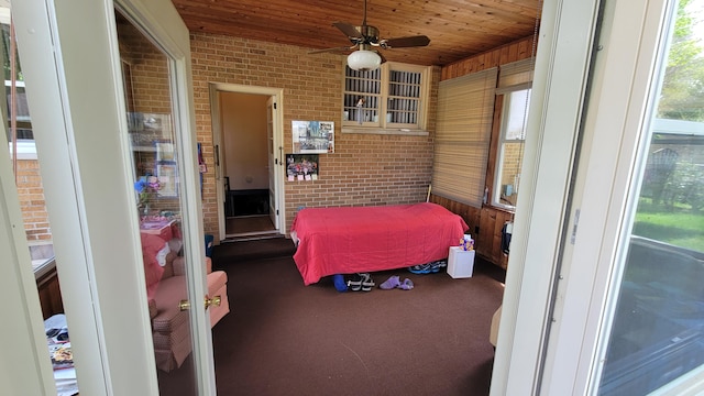 bedroom featuring multiple windows, ceiling fan, and brick wall