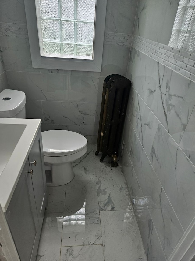 bathroom with radiator heating unit, vanity, toilet, and tile walls