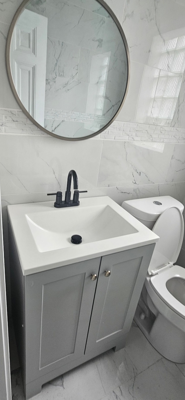 bathroom featuring vanity, toilet, and tile walls