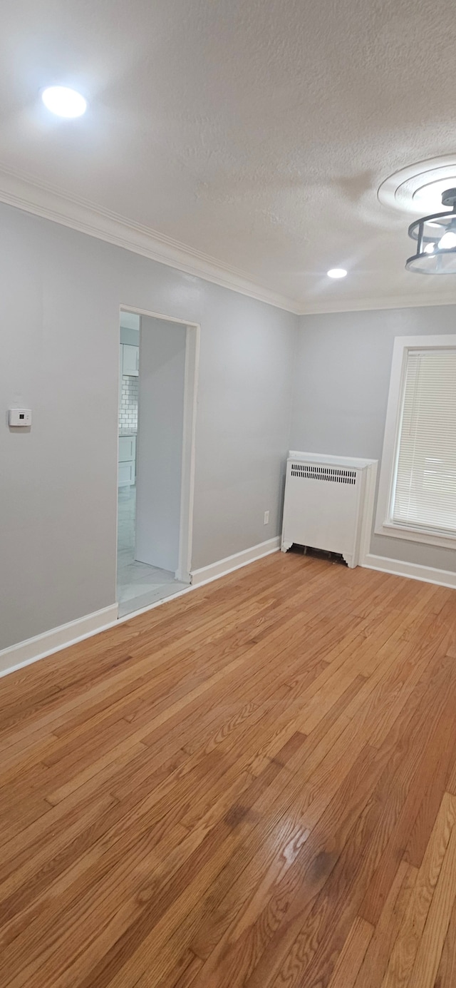 empty room featuring radiator, ornamental molding, a textured ceiling, and light wood-type flooring