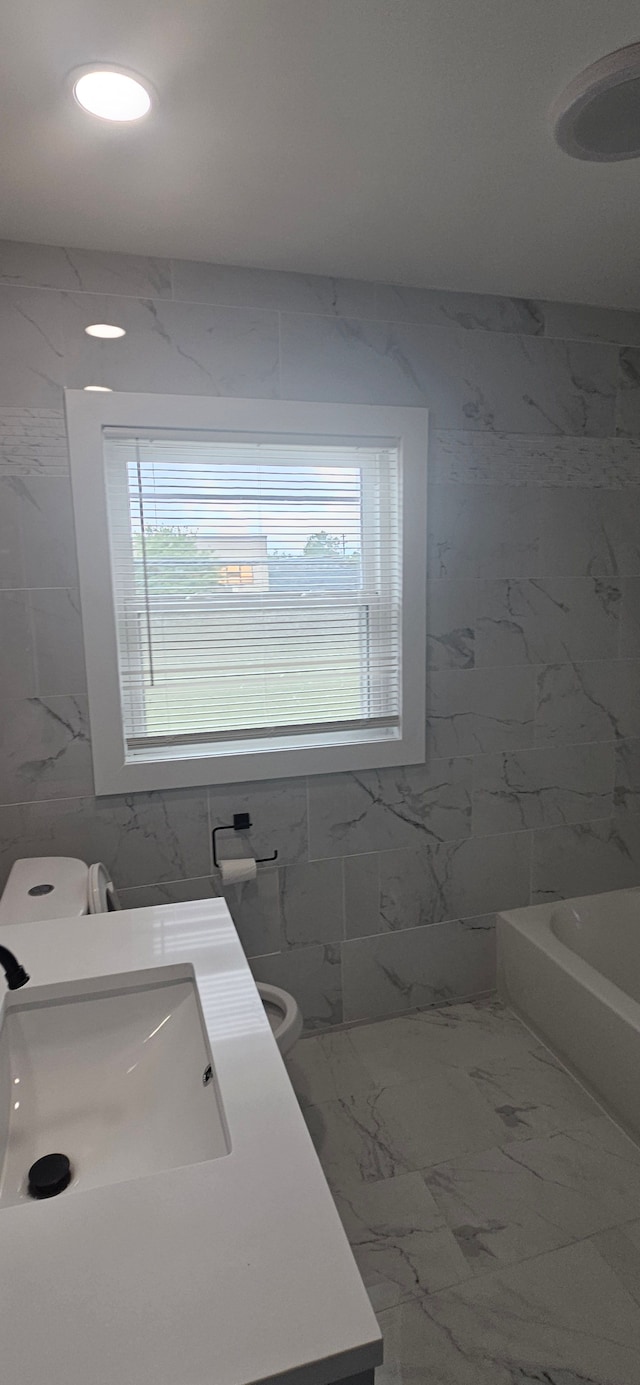 bathroom with vanity, toilet, a wealth of natural light, and tile walls