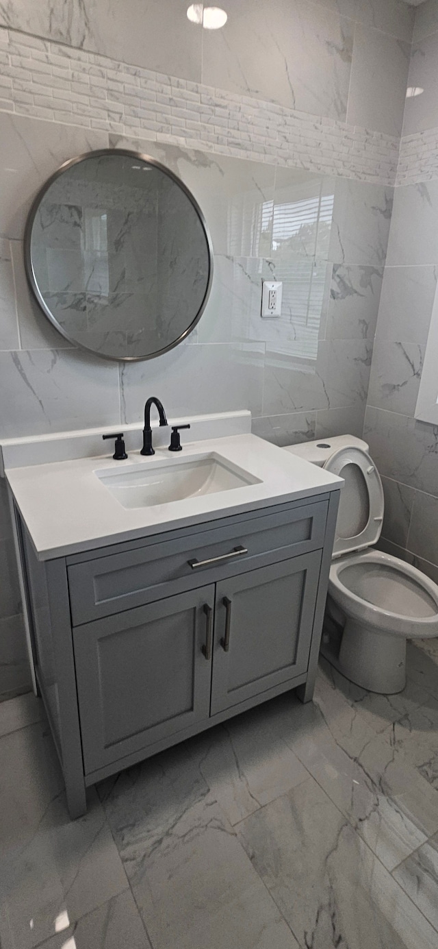 bathroom featuring vanity, toilet, and tile walls