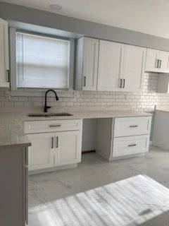 kitchen with tasteful backsplash, white cabinetry, and sink