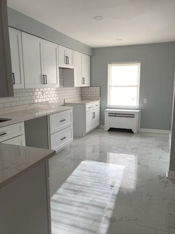 kitchen featuring white cabinets, radiator heating unit, tasteful backsplash, and light stone countertops