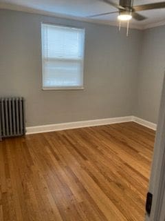 unfurnished room featuring hardwood / wood-style flooring, ceiling fan, radiator heating unit, and ornamental molding