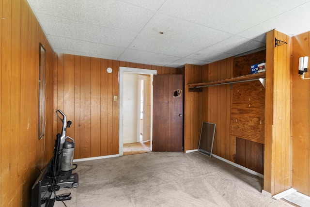 misc room with a drop ceiling, wood walls, and light colored carpet