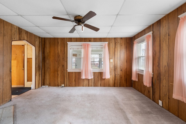 carpeted spare room featuring wood walls, a drop ceiling, and ceiling fan