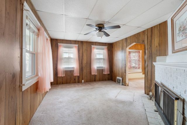 unfurnished living room with ceiling fan, light colored carpet, wood walls, and a brick fireplace