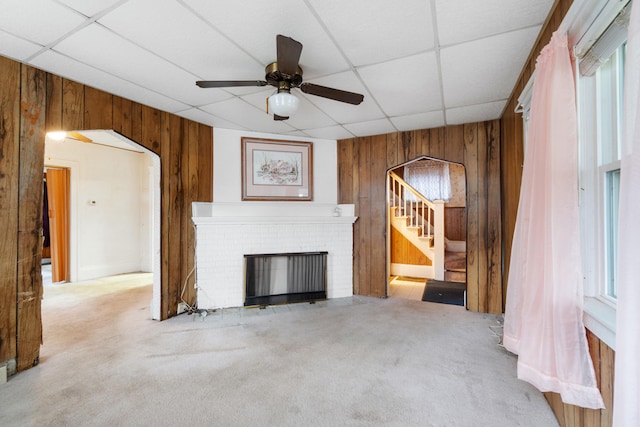 unfurnished living room with a drop ceiling, carpet floors, a fireplace, and wooden walls