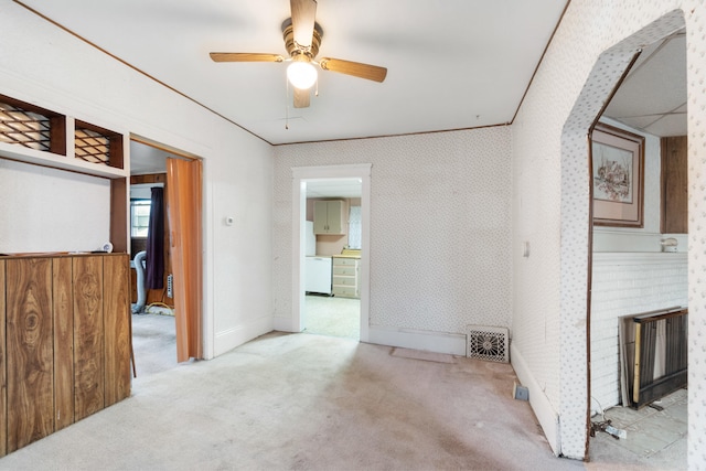 empty room with ceiling fan, a fireplace, light colored carpet, and crown molding