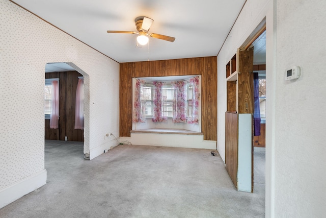 carpeted spare room featuring wooden walls, ceiling fan, and a healthy amount of sunlight