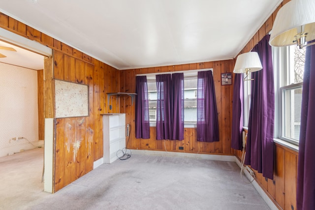 empty room with light carpet, a healthy amount of sunlight, and wood walls