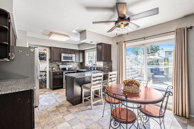 kitchen with decorative backsplash, appliances with stainless steel finishes, dark brown cabinetry, sink, and a kitchen island