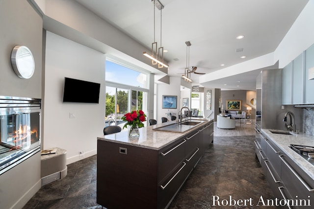 kitchen featuring light stone counters, sink, an island with sink, and ceiling fan