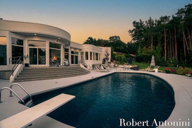 pool at dusk with a diving board and a patio area