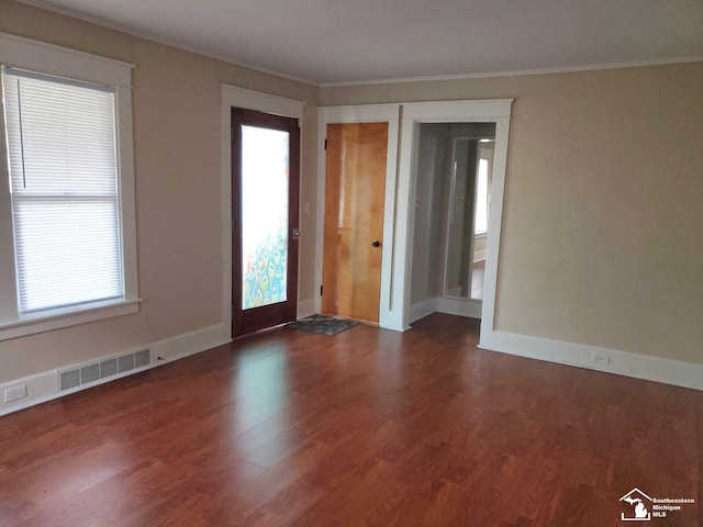 empty room featuring a healthy amount of sunlight, dark hardwood / wood-style flooring, and crown molding