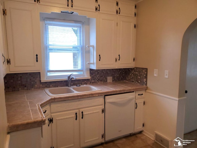 kitchen featuring tile countertops, backsplash, white dishwasher, white cabinets, and sink