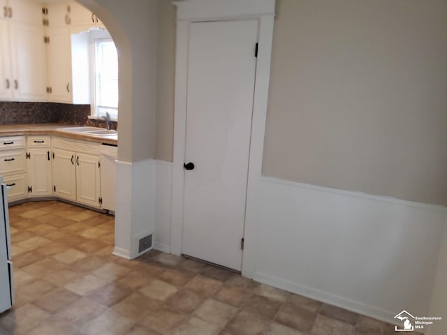 kitchen with dishwasher, backsplash, white cabinetry, and sink