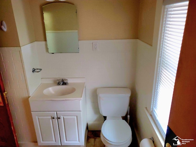 bathroom with vanity, a healthy amount of sunlight, toilet, and tile walls