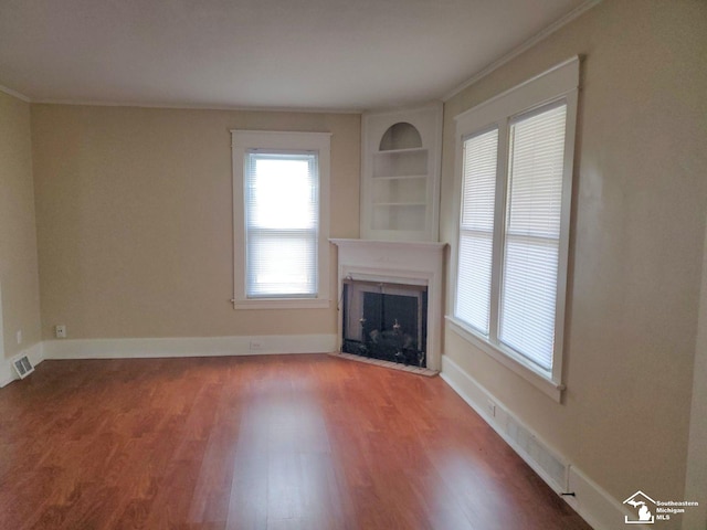 unfurnished living room with hardwood / wood-style floors, crown molding, and built in shelves